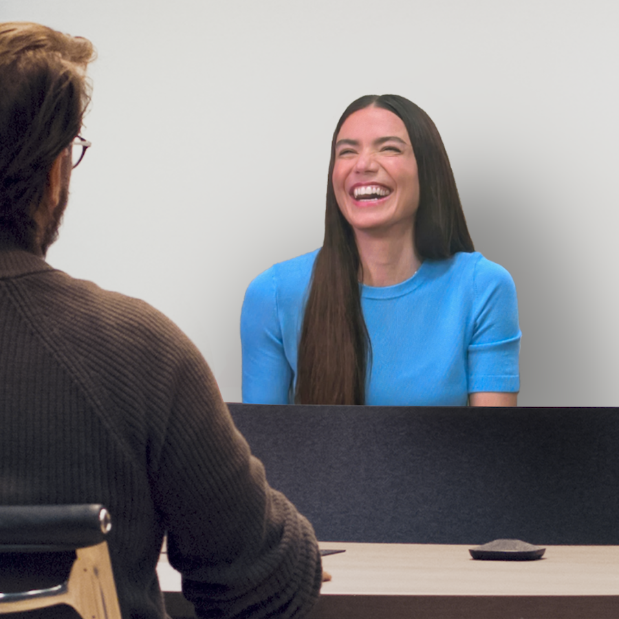 A person is smiling from a Beam display. The shoulder of the person on the other side of the Beam display is visible.