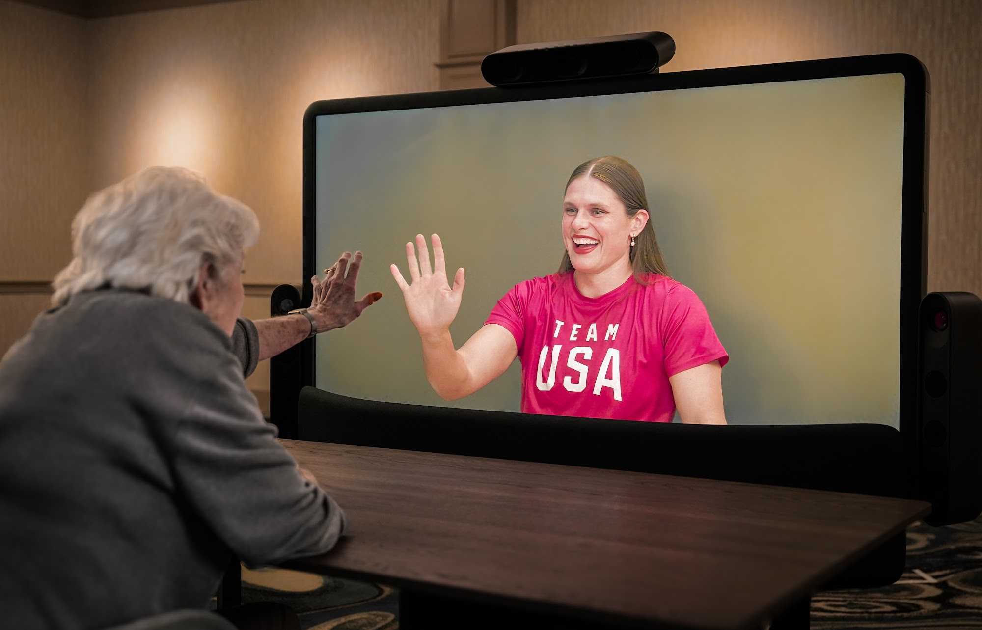 Ilona Maher proudly waves hello while using a Starline device. Oma Lily, visible on the screen of the starline device, waves back with excitement
